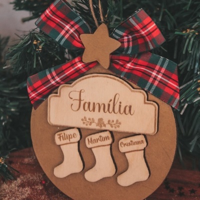 Decoração de Natal em madeira com laço xadrez vermelho, verde e branco, estrela e botinhas com nomes gravados penduradas num ramo de pinheiro.