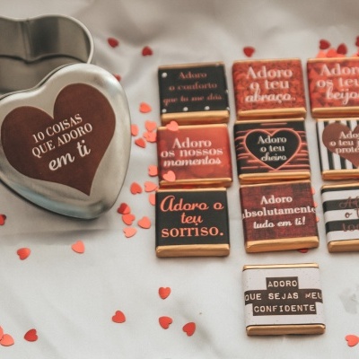 Biscoitos decorados com mensagens de afeto em várias cores e formatos, dispostos sobre tecido branco com corações vermelhos.