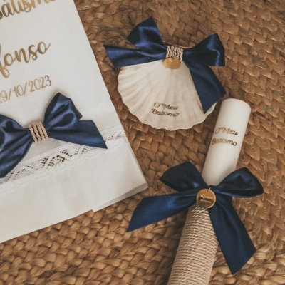 Conjunto para batismo com vela, concha e toalha branca decorados com laços azuis e pendentes dourados