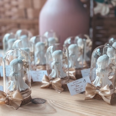 Figuras de anjinhos em copos de vidro com laços dourados sobre mesa de madeira