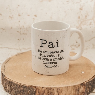 Caneca branca com texto em preto 'Pai Eu sou parte da tua vida, e tu és toda a minha história! Amo-te' sobre tronco de madeira