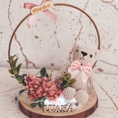 Arranjo decorativo com ursinho de crochê, flores cor de rosa e placa AVÓS em estrutura circular sobre base de madeira
