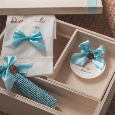 Caixa branca de madeira com toalha, vela e sabonete decorados com laços azuis.