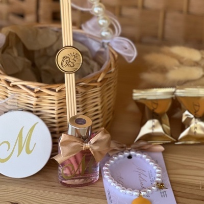 Cesto de verga com presentes para madrinha de casamento, incluindo ambientador, chocolates, espelho, pulseira e etiqueta.