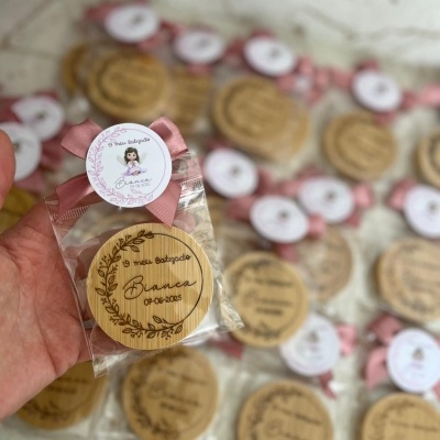 Chaveiro redondo de madeira personalizado para batizado com fita rosa e etiqueta com ilustração.