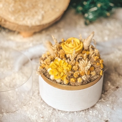 Vela decorativa amarela em recipiente branco com flores secas amarelas.