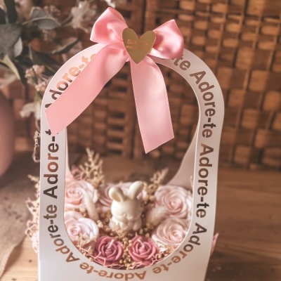 Arranjo decorativo rosa com figura de coelho em embalagem branca com alça e laço