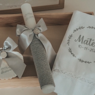 Conjunto de batizado com vela, toalha branca bordada e sabonete com laços cinza numa caixa de madeira