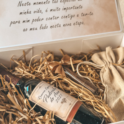 Conjunto de presente com garrafa de vinho, gravata e saco de tecido em caixa branca com palha de papel.