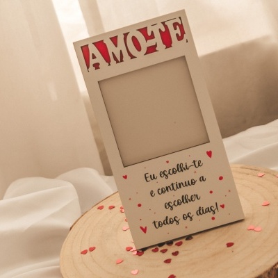 Porta-retratos branco com corte e texto amoroso colocado sobre tronco de madeira com cortinas ao fundo