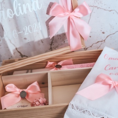Caixa de lembranças para batizado com toalha branca, laços rosa e vidro transparente com texto branco.