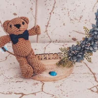 Urso de malha castanho sentado em baloiço decorado com flores azuis