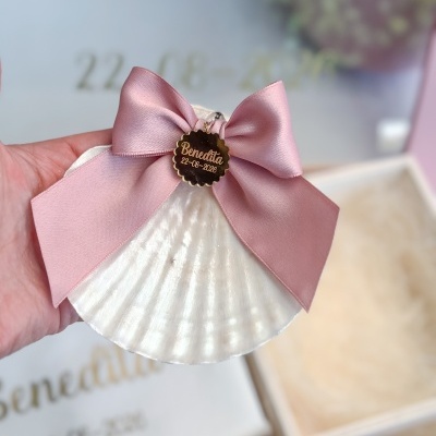 Concha branca com laço rosa e medalha dourada com texto Benedita 22-08-2026