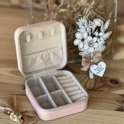 Estojo de joias rosa claro com interior de veludo bege aberto numa mesa de madeira com decoração floral atrás