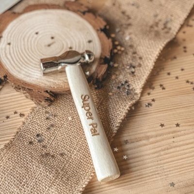 Martelo pequeno com cabo de madeira e cabeça metálica sobre tecido rústico e superfície de madeira.