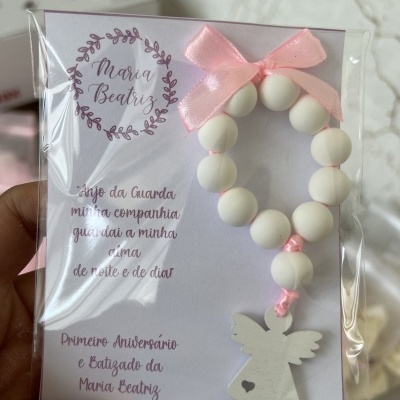 Pulseira branca de contas com anjo pendurado e laço rosa em embalagem transparente
