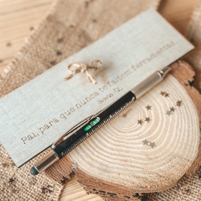 Caneta preta e prateada sobre madeira redonda com cartão cinza e tecido de juta