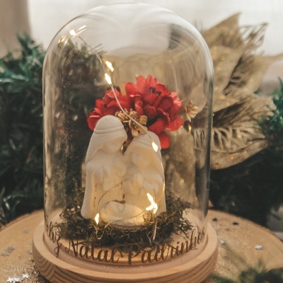 Presépio decorativo com três reis magos dentro de campânula de vidro sobre base de madeira com luzes e flores vermelhas