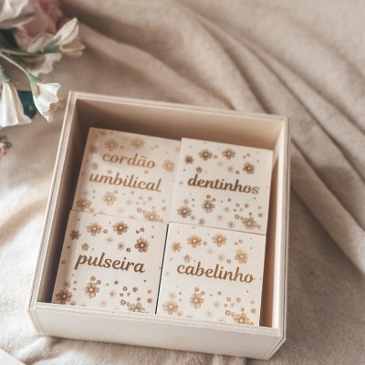 Caixa de madeira com quatro pequenas caixas decoradas com flores e texto relacionado a lembranças de bebé