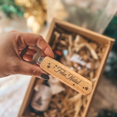 Abre-garrafas de madeira claro com 'Feliz Natal' gravado e caixa de oferta