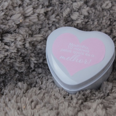 Caixa branca em forma de coração com rótulo rosa e texto em cima sobre tecido felpudo castanho claro