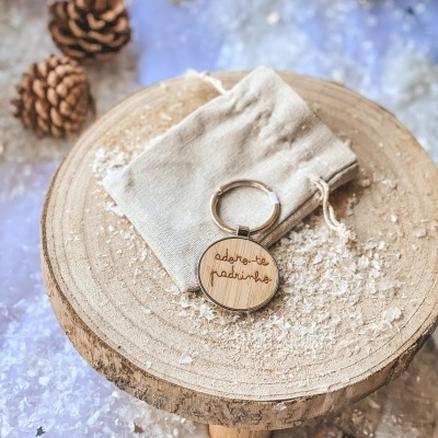 Chaveiro de madeira gravado com texto 'adoro-te padrinho' sobre saco de pano e suporte de madeira com decoração de inverno