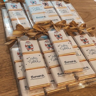 Pacotes de chocolate com rótulos de Natal personalizados e laços dourados sobre madeira