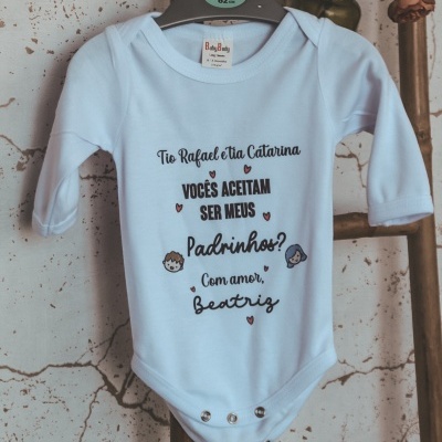 Body de bebé azul claro com texto impresso, pendurado numa cabide numa escada rústica