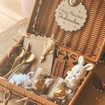 Cesto rústico com chávenas, colheres douradas, chaveiros, coelho decorativo e cartão de Feliz Páscoa Padrinho.