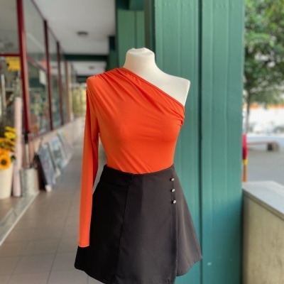 Maniquim com blusa laranja assimétrica de manga longa e saia preta com botões em corredor coberto