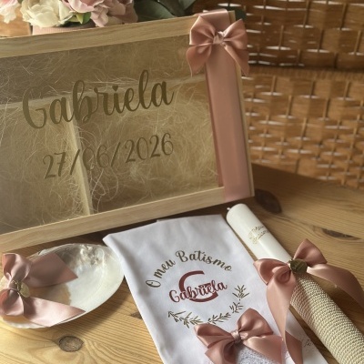 Conjunto de batismo com caixa de madeira, vela branca, toalha bordada e concha com fita rosa.