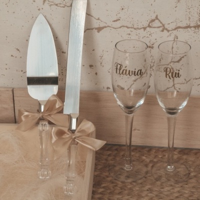 Utensílios para bolo com laços e duas taças gravadas em vidro sobre madeira