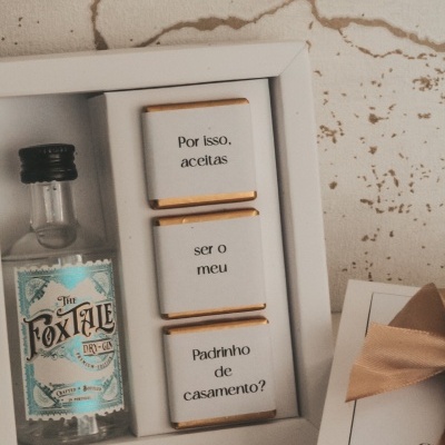 Caixa branca com garrafa de gin e chocolates com texto pedido para ser padrinho de casamento
