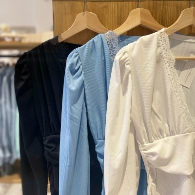 Três blusas para mulher nas cores preta, azul clara e branca penduradas em cabides de madeira