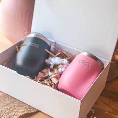 Conjunto de duas canecas térmicas preto e rosa com frases, em caixa branca com decorações.