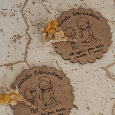 Dois cartões redondos de papel castanho com ilustração e texto, decorados com flores secas sobre superfície manchada clara