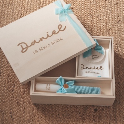 Caixa de madeira branca decorada com laço azul claro e texto gravado, contendo vela com laço azul e moldura com texto