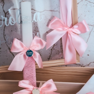 Vela decorativa branca com fita rosa e moldura com laço rosa num fundo branco texturizado