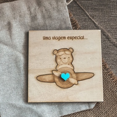 Quadro em madeira clara com ursinho piloto de avião e coração azul, texto Uma viagem especial...