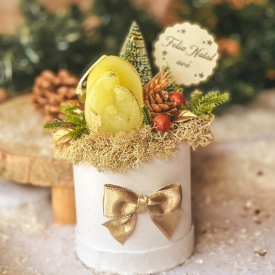 Arranjo de Natal com vela, pinha, frutos vermelhos e laço dourado em vaso branco.
