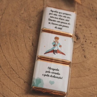 Três barras de chocolate com frases em português e ilustrações, sobre superfície de madeira clara
