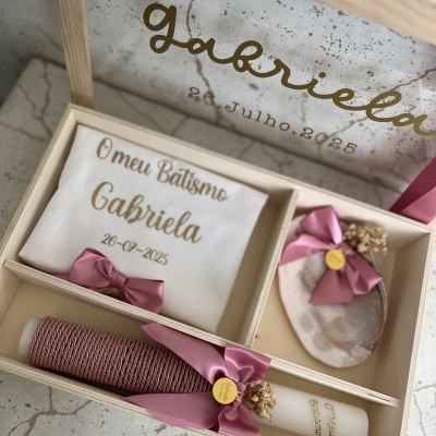 caixa de madeira clara com toalha branca, duas velas e saco decorativo com laços rosa