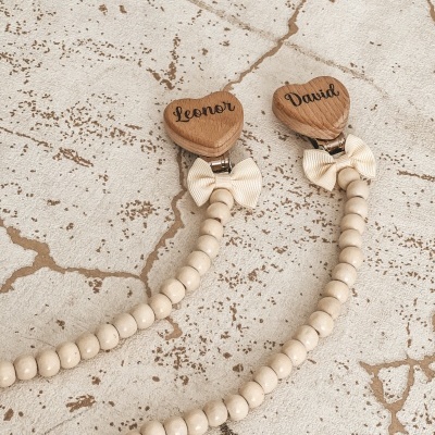 Prendedores para chuchas com contas de madeira, laços creme e peças de madeira em forma de coração com os nomes Leonor e David