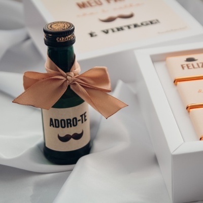 Conjunto de presente com garrafa pequena com rótulo e caixa branca com barras de chocolate sobre tecido branco