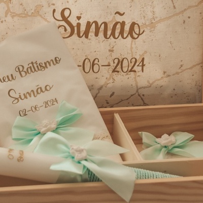 Conjunto de batismo com toalha branca bordada e vela com laço verde-água numa caixa de madeira