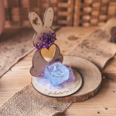 Figura decorativa coelho madeira com vela azul e flores secas sobre base madeira