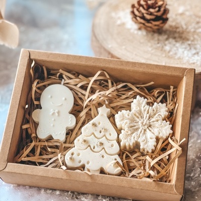 Velas brancas natalícias numa caixa de cartão com decoração de palha e neve falsa.