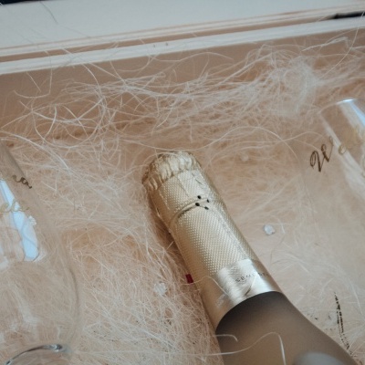 Caixa de madeira com garrafa de champanhe dourada e duas taças de vidro com inscrições