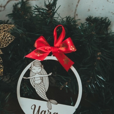 Enfeite de Natal branco redondo com desenho de sereia e nome Yara com fita vermelha pendurado em pinheiro