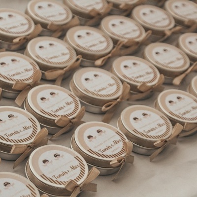 Caixas redondas bege com tampa transparente etiquetadas com 'Tania & Nini' organizadas em fileiras sobre mesa clara